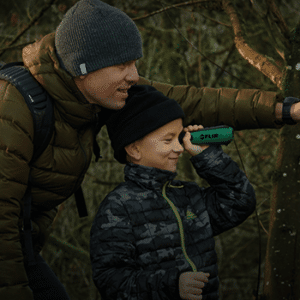 Photo of a boy looking through a Teledyne FLIR Scout TK thermal monocular while his father stands behind him pointing in the direction he is looking.