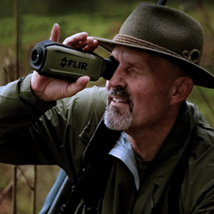 Man in a fedora hate seen looking through a Teledyne FLIR Scion OTM outdoor thermal monocular.