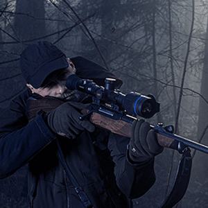 Man shown taking aim through a Pulsar Thermion 2 Pro attached to a bolt-action rifle.